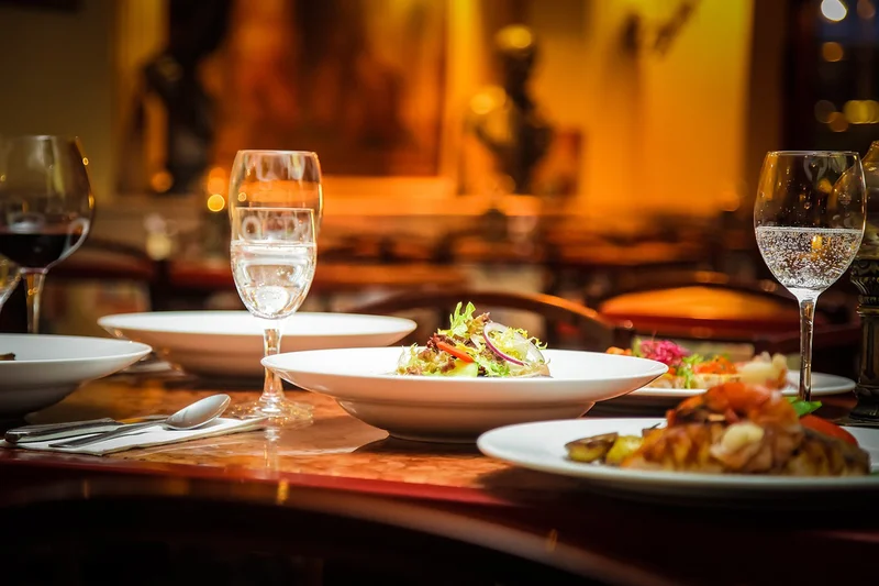 Tisch mit mehreren Tellern und Vorspeise-Salat, gefüllten Weingläsern und Besteck in warm beleuchteter Restaurantumgebung