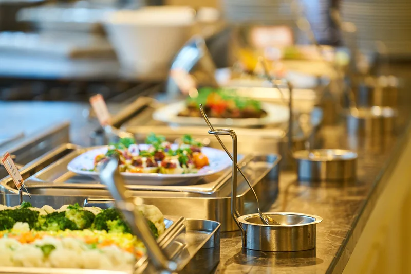 Metallene Warmhaltebehälter mit Gemüse, Schalen und Servierlöffeln auf einer Buffettheke
