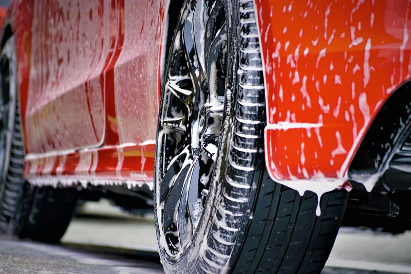 Nahaufnahme eines rot lackierten Fahrzeugs mit schäumender Autowäsche an Felge und Kotflügel